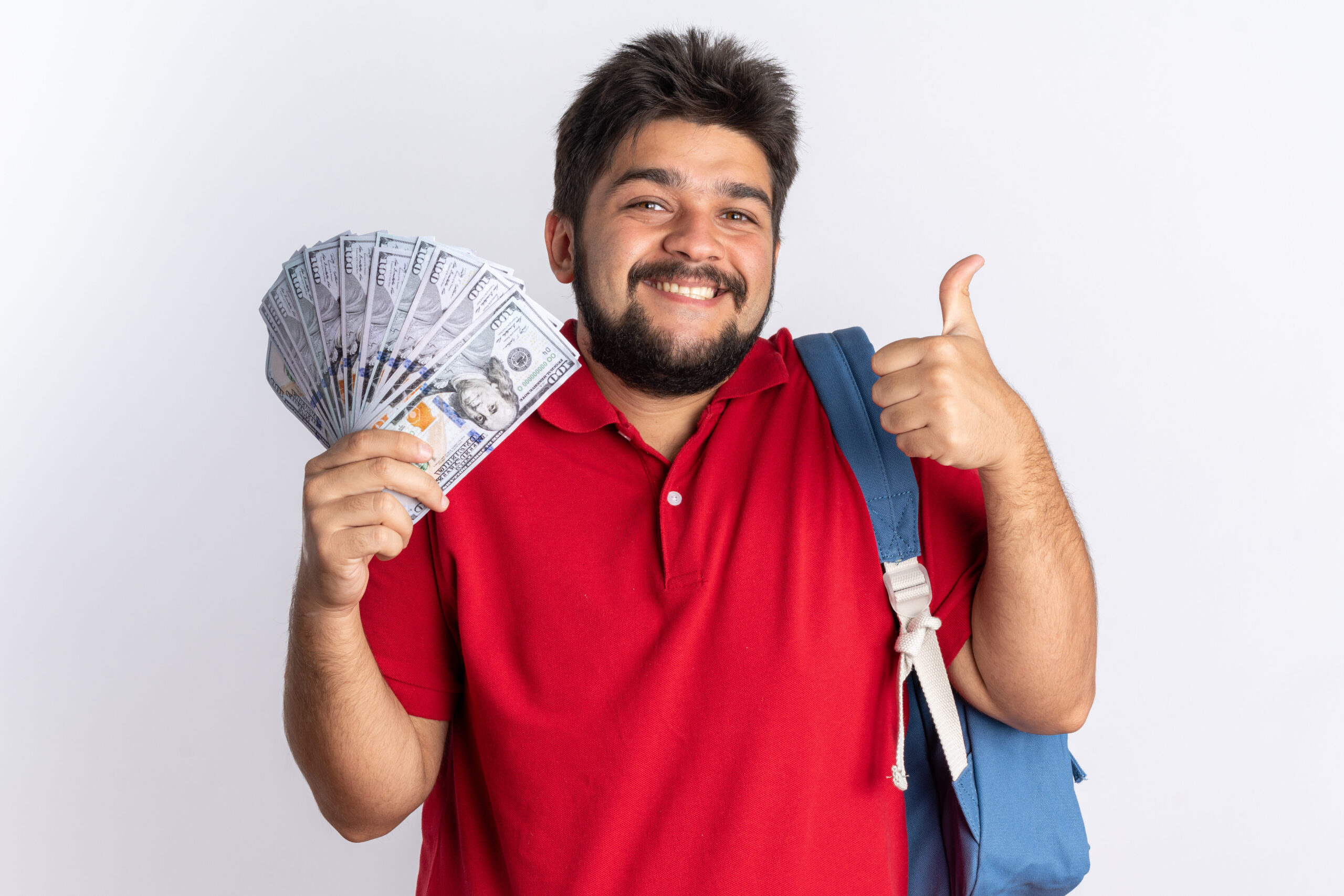 young bearded student guy in red polo shirt with backpack holding air tickets and globe happy and positive looking at camera showing thumbs up smiling standing over white background
